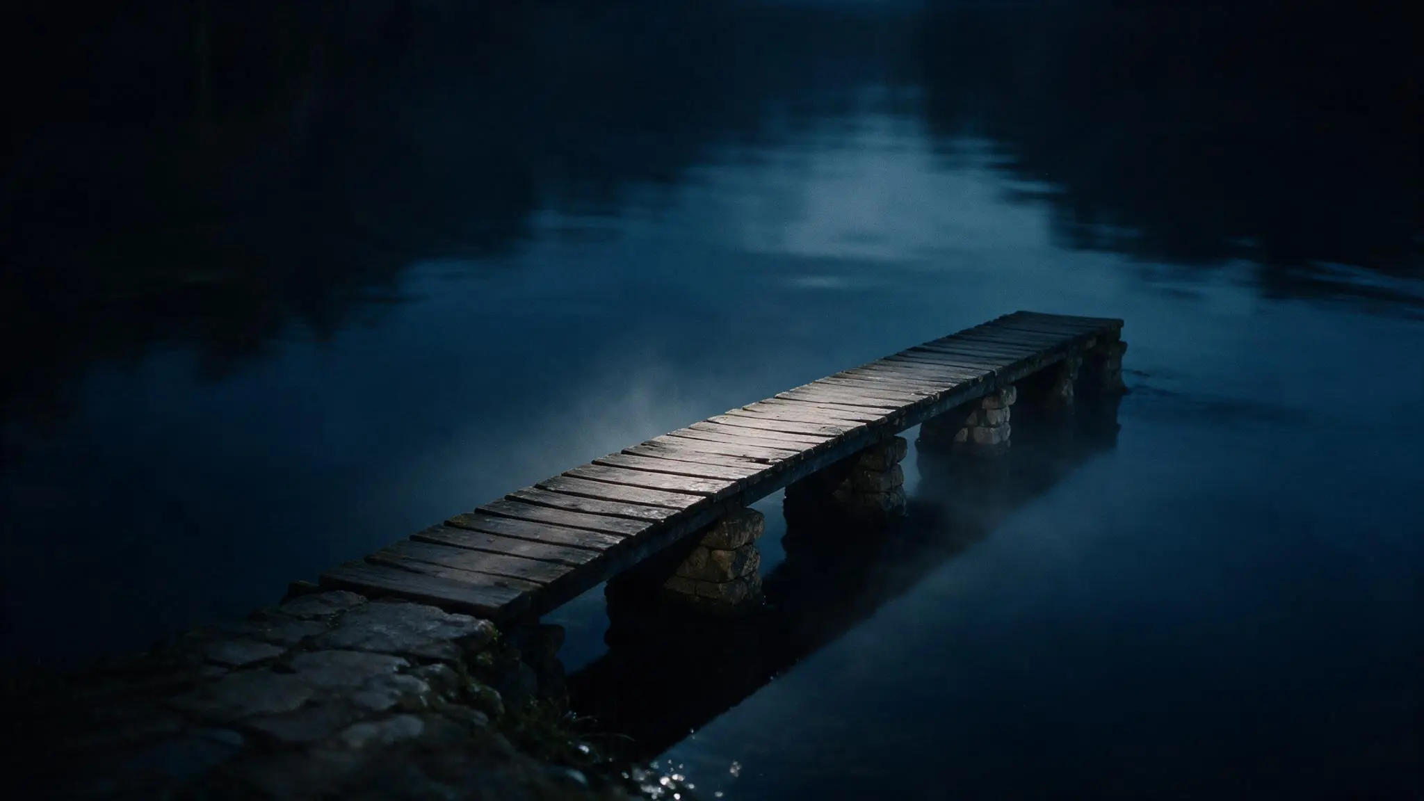 A simple low timber and stone bridge crossing dark water before dawn, with low mist around its supports.