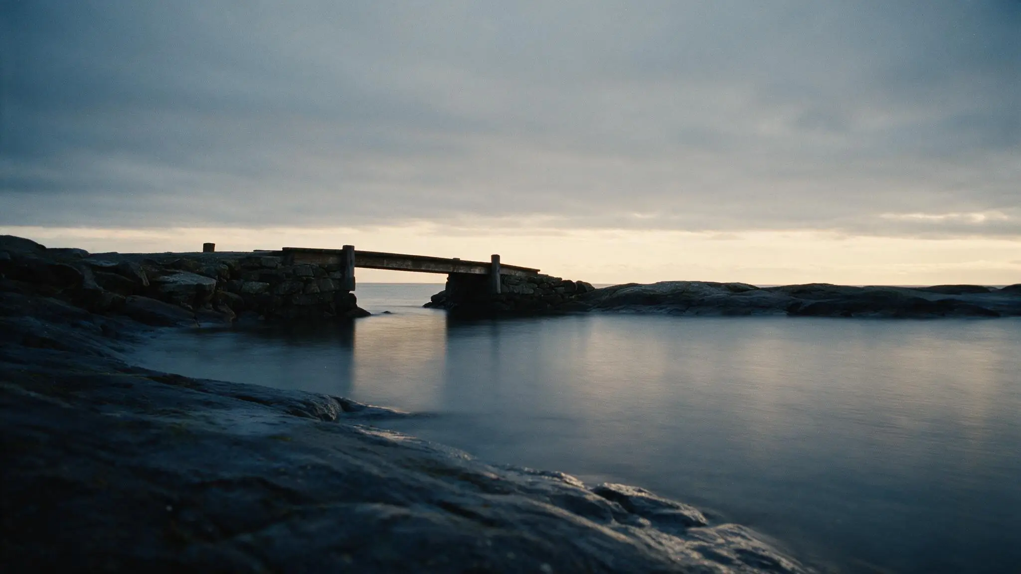 The bridge arriving at a quiet rock shore in calm early morning light, the water settled.